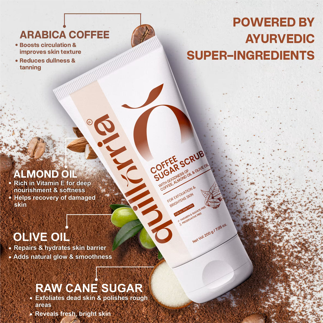 Quillorria Coffee and Sugar Scrub product tube surrounded by raw ingredients: Arabica coffee grounds, almond oil, olive oil, and raw cane sugar. Text highlights coffee scrub benefits for circulation, deep nourishment, and skin polishing.